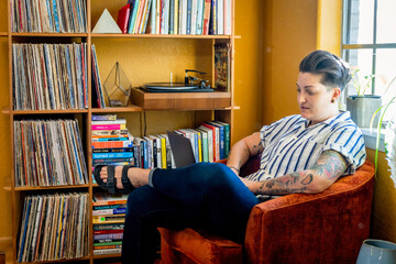 Masculine looking woman working on laptop in home next to bookshelf