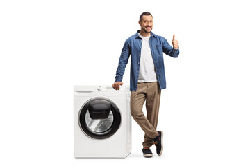 Young man standing next to a washing machine and showing thumbs up