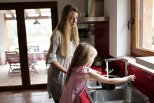 Mother And Daughter Washing Vegetables In Kitchen