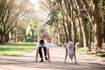 Wall Mural - Young araian couple in sportswear standing in starting position at green park and getting ready for jogging. Sport, family and motivation concept.