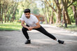 © sofiko14 - Active male athlete in sport clothes stretching legs before morning run at green park. Handsome hindu guy warming up outdoors. Sport activity concept.