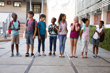 Wall Mural - Group of diverse students with backpacks smiling while looking at each other at school