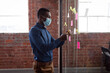 © wavebreak3 - African american businessman wearing face mask brainstorming, reading memo notes on glass wall