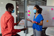 © wavebreak3 - Diverse male and female colleague in face masks discussing paperwork in office