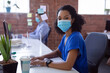 © wavebreak3 - Portrait of african american businesswoman in face mask at desk with hygiene screen in office