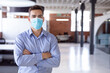 © wavebreak3 - Portrait of caucasian businessman wearing face mask standing in office with arms crossed