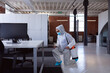 © wavebreak3 - Cleaner wearing ppe suit, glasses and mask disinfecting office workspace