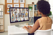 Woman having online business conference or video call staff meeting. Young black lady sitting at office desk with computer talking to team of coworkers who work from home or have hybrid work schedule