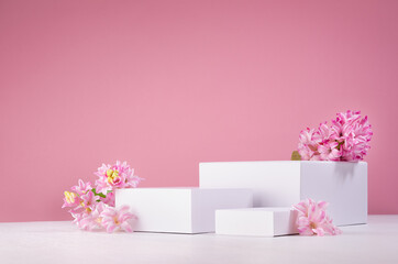 Wall Mural - Set of three white podiums for presentation cosmetics produce with fresh spring flowers on pastel pink background.