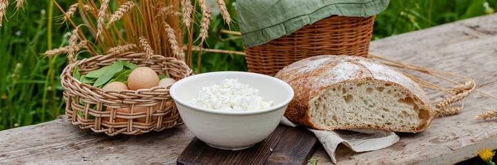 Concept of natural organic products from the local farm. Homemade bread, fresh milk, eggs, cottage cheese. Simple food. Wooden background, outdoors. Close up, copy space. Banner