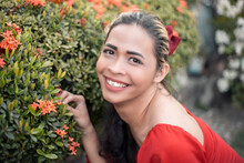 A Happy And Upbeat Transgender Woman Inspects Some Santan Flowers. Of Southeast Asian Descent. Garden Setting.