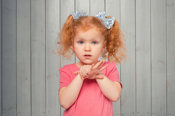 Cute timid redhead little girl 4-6 years old in casual pink t shirt standing shy and silly, looking at camera blushing