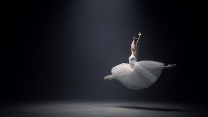 Gorgeous woman soaring in ballet dress on stage. Ballerina dancing indoors.