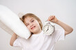 © Maria - A little sleepy girl hugs a pillow and an alarm clock on a white background.