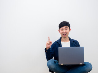 Asian man with laptop sitting on the chair get idea point finger up on white wall background