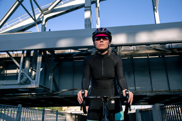 Wall Mural - Portrait of a bicycling woman in helmet and glasses illuminated by the sun at morning trainings in the city.