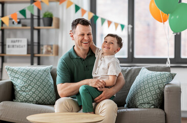 Wall Mural - family, fatherhood and people concept - portrait of happy smiling father and little son hugging at home birthday party