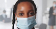 © nimito - Afro young businesswoman wearing protective mask standing in modern office and looking at camera