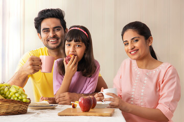 A HAPPY FAMILY LOOKING AT CAMERA WHILE HAVING BREAKFAST	