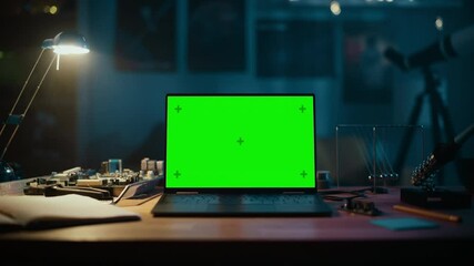 Laptop Computer Standing on a Table with a Green Screen Chromakey Mock Up Display. Cozy Empty Room with a Lamp, Circuit Board, Newton's Cradle and Tools on the Table. Zoom In Footage.