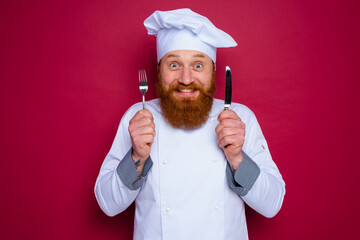 Wall Mural - happy chef with beard and red apron holds cutlery in hand