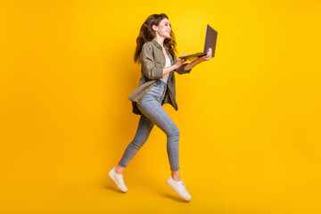 Wall Mural - Full length photo of charming sweet young lady wear brown shirt jumping looking modern gadget isolated yellow color background