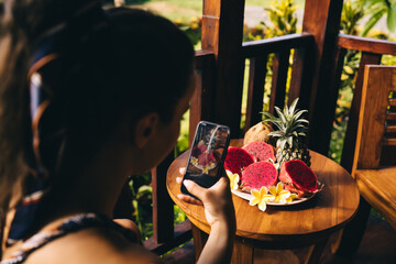 Anonymous woman taking photo of exotic fruits on terrace