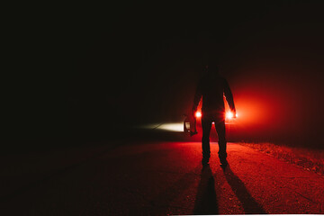 maniac killer near the car at night. silhouette of a man with an ax in his hand at night in a fog.