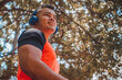 © Julaix - athletic man of Latin origin after training with a tough attitude with a yellow sweater or walks with a hood and a bad man's face, Venezuelan model in sports in the park with blue music headphones