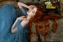 Red-haired Beauty Languidly Lies On A Table With Fruits