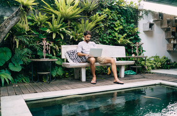 Wall Mural - Focused man working on laptop on poolside