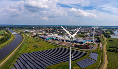 Panorama of wind turbines, water treatment and bio energy facility and solar panels part of sustainable industry in Dutch flat river landscape against a blue sky. Aerial circular economy concept.