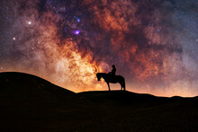 Silhouette Of A Lone Rider On A Horse Standing On A Hill In The Starry Night. Behind Him Is The Beautiful Bright Milky Way Galaxy.