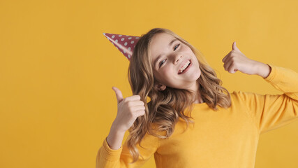 Wall Mural - Positive teenage girl in party hat looking happy keeping thumbs