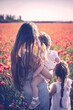 Little girls and mother in white dresses and wreathes walking of poppies on poppy field at warm summer sunset.