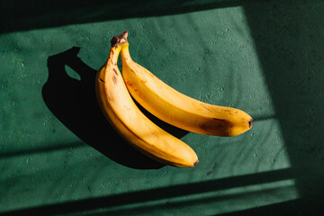 Bananas on a green background. Summer abstract creative photography with sun light and shadows.