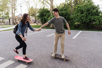 Young Caucasian couple teaching to each others while practicing skating, lifestyle extreme outdoor activity. People lifestyle recreation. Success team skating holding hands