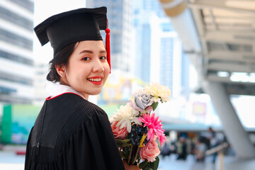 Portrait of happy smiling graduated student, Asian woman with flower bouquet looking at camera so proud on commencement day, people celebrating successful education on graduation day when have finishe