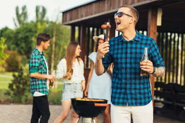 Young happy man in sunglasses having a group of friends having a barbecue with beer drinks having a rest in nature