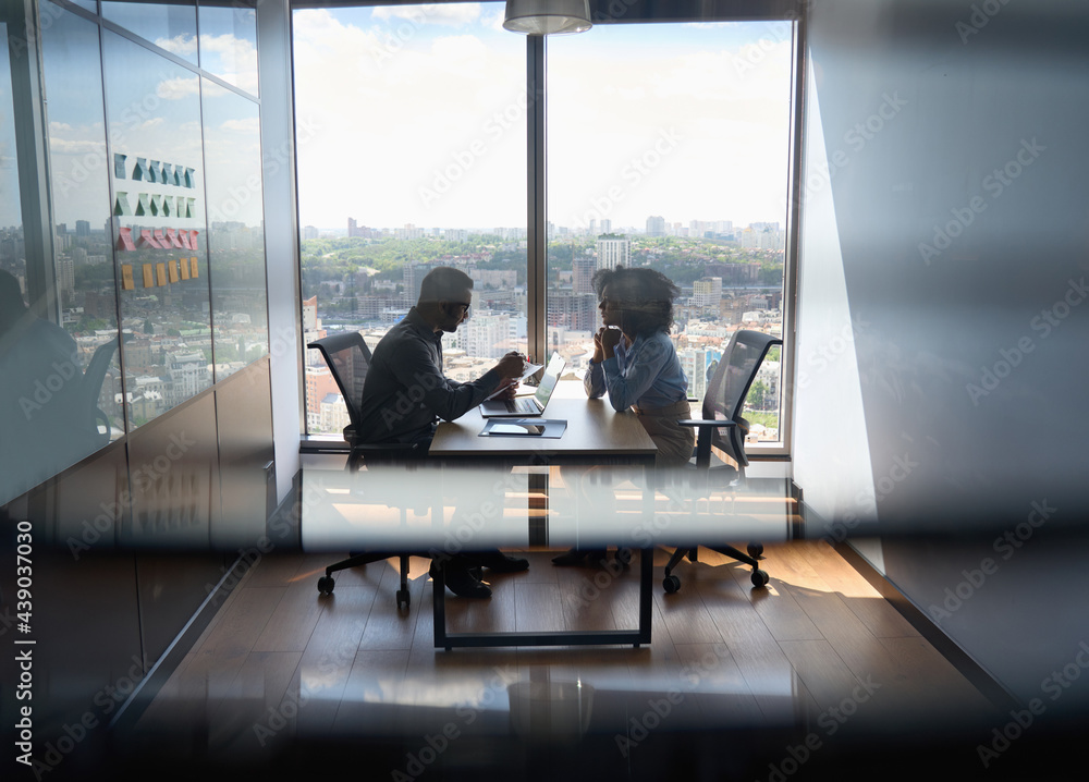Young indian businessman ceo hr director having interview hiring for job with female African American attorney sitting in office at panoramic view window. Shot through jalousie glass. - obrazy, fototapety, plakaty 
