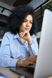 © insta_photos - Young serious concerned African American businesswoman sitting at desk looking laptop computer in contemporary corporation office. Business technologies concept. Vertical portrait.