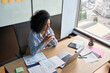 © insta_photos - Young African American businesswoman ceo sitting at desk having videocall on yearly financial report with colleagues using laptop near panoramic window in contemporary corporation office.