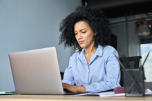 Young Serious African American Female Ceo Lawyer Businesswoman Sitting At Desk Working Typing On Laptop Computer In Contemporary Corporation Office. Business Technologies Concept.