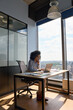 © insta_photos - Concentrated African American executive top manager sitting at desk working typing on laptop computer in modern corporate office with panoramic view. Business technologies concept. Vertical shot.