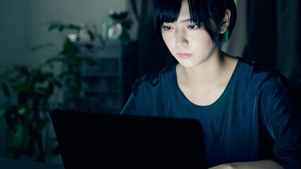 暗い部屋でパソコンを使う女性