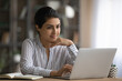 © fizkes - Confident young indian woman worker sit at office table by laptop search data browse corporate network for business news. Smiling female freelancer read document online correspond with client in chat