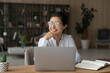 © fizkes - Young indian lady scientist in glasses work on pc do research sit by desk at home in library think of success distracted from screen. Teen female student relax from studying visualize good exam result