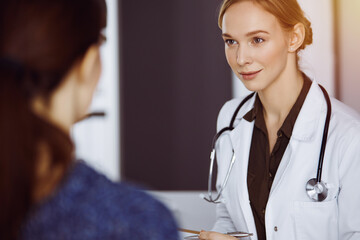 Cheerful smiling female doctor and patient woman discussing current health examination while sitting in clinic. Medical service in hospital. Medicine concept