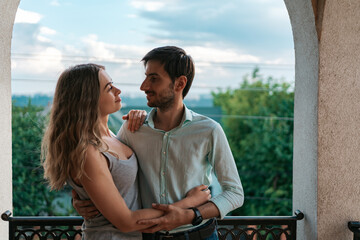 Man embracing wife at balcony. Relaxed couple enjoy day and good news. Happy young family