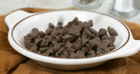 Poster - Pouring milk chocolate chips into a small bowl super slow motion